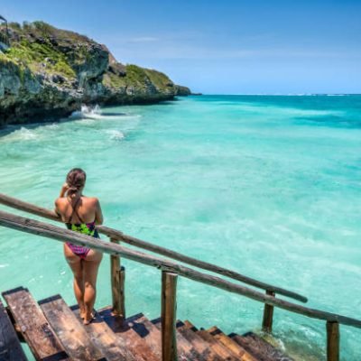 Young woman standing on a wooden pier, contemplating the crystal-clear turquoise water of Mtende Beach, a beautiful tropical paradise in Zanzibar, Tanzania
