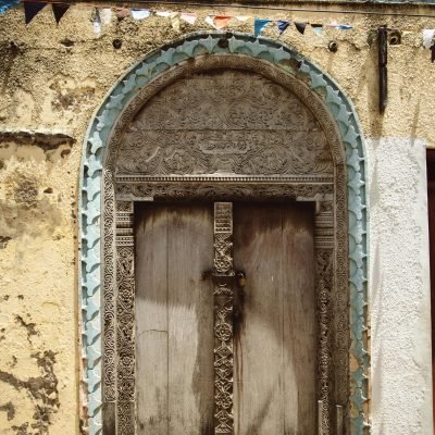 Ornate wooden door in a historical building with intricate carvings and textured facade.