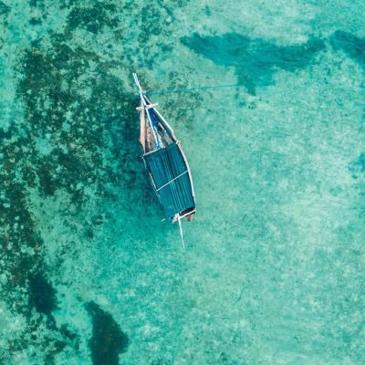 Drone shot of a boat floating in clear turquoise waters of Zanzibar, Tanzania. Serene and scenic top view.